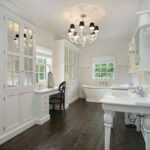 A white bathroom with twin console sinks, a freestanding tub, subway tile and dark hardwood floors.