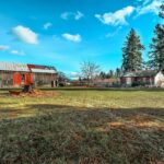 A rustic barn and farmhouse sit amid open pasture land with trees and mountains in the rural Idaho landscape.