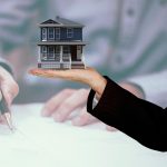 A hand giving or signing a real estate contract document, representing a property sale, mortgage, or rental agreement.
