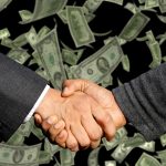 Two people shaking hands over a business agreement, symbolising a commercial deal or contract.