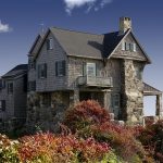 Large stone house with masonry facade set within a landscape.