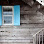 Wooden house exterior showing shuttered windows, a facade with architectural details, and an exterior staircase.
