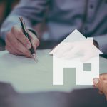 A hand holding a pen signing a home purchase contract on paper.