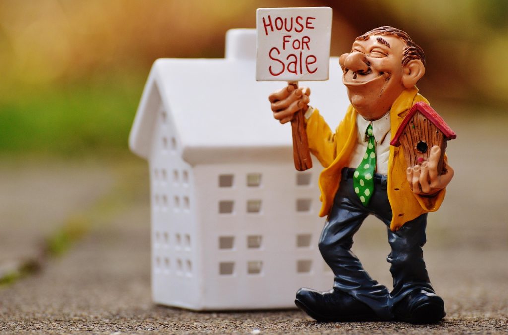 A person in a necktie holds a small birdhouse figure, representing a real estate profession.