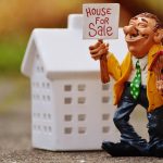 A person in a necktie holds a small birdhouse figure, representing a real estate profession.