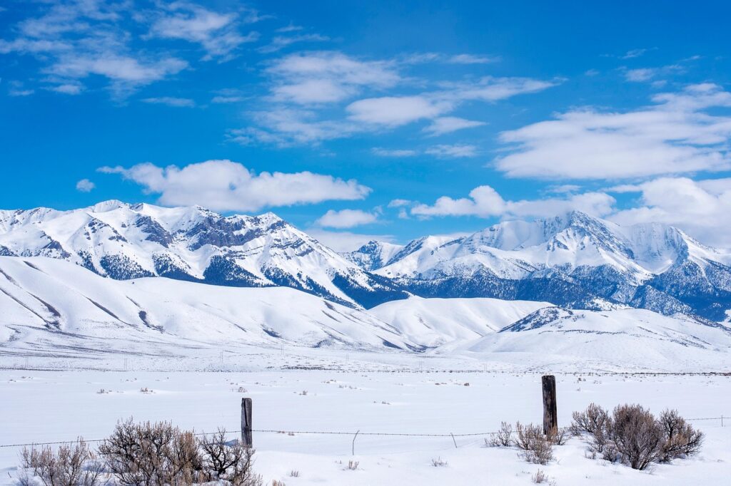 Snow-covered mountains rise behind a ranch fence along US Highway 93 in Idaho.