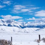 Snow-covered mountains rise behind a ranch fence along US Highway 93 in Idaho.