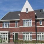 A newly constructed home with a steep roofline alongside an older resale property.
