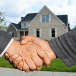 A real estate agent handing over property documents during a house purchase transaction.